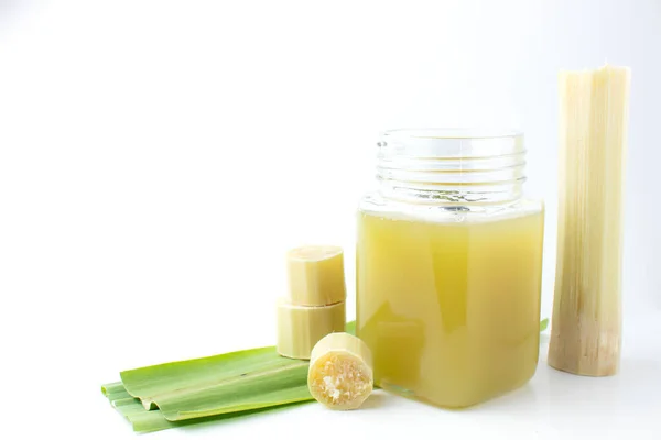 Temiz bardakta taze sıkılmış şeker kamışı suyu ve beyaz arka planda kesilmiş kamış..