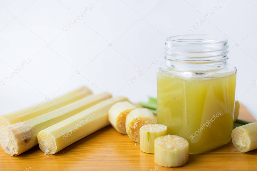 Fresh squeezed sugar cane juice in clear glass with cut pieces cane on white background.