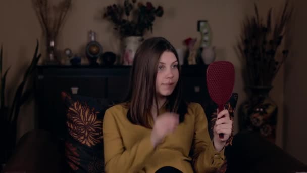 Gros plan Jeune jolie femme, d'apparence caucasienne, assise dans un fauteuil et redresse ses cheveux en regardant dans le miroir. Concept de beauté . — Video