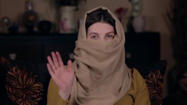 Arap görünümlü genç, güzel bir kadın çarşaflı bir koltukta oturur ve video bloğunu yazar. Sosyal Medya Günlük Kavramı.