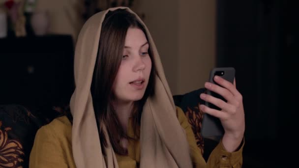 Una joven mujer cristiana bonita con un pañuelo en la cabeza, de aspecto caucásico, se sienta en un sillón y graba un video vlog. Concepto de Blogging en Redes Sociales . — Vídeos de Stock