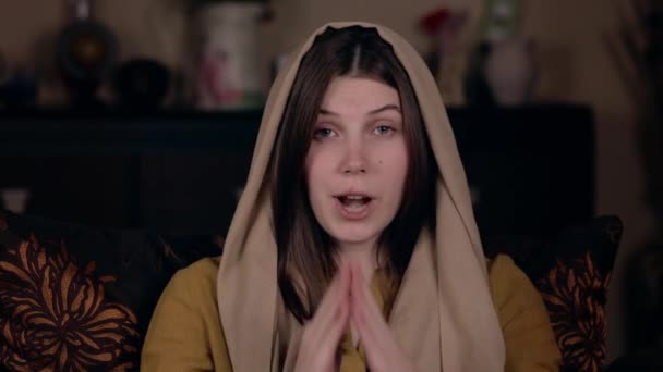 머리에 스카프를 두른 예쁘고 기독교적 인 젊은 여성, 외모는 카프카스 인, 의자에 앉아 비디오 녹화를 하며 온라인 기도를 한다. 소셜 미디어 블로 깅 개념. — 비디오