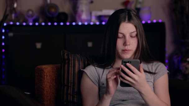 Donna caucasica che utilizza smartphone e sbadiglia mentre seduto sulla sedia a casa. Tecnologia e concetto di relax . — Video Stock