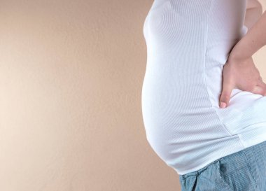 Güzel hamile bir kadının karnına dokunuşunun kırpılmış görüntüsü.