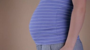 Mavi tişörtlü hamile bir kadının göbeğinin yakın plan görüntüsü. Broşürlerde yazılı olan broşürleri tutuyor ve evet. Hamilelik sırasında seyahat kavramı.