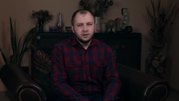 L'influent Bearded Young, un blogueur d'apparence européenne, est assis sur une chaise en chemise à carreaux et appelle très émotionnellement à s'abonner à sa chaîne. Social Media Blogging Concept . — Video