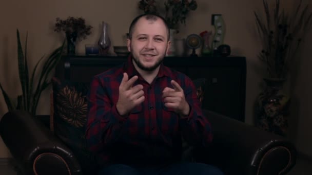 El influyente Joven Barbudo, un blogger, de apariencia europea, se sienta en una silla con una camisa a cuadros y pide escribir comentarios bajo el video. Concepto de Blogging en Redes Sociales . — Vídeos de Stock