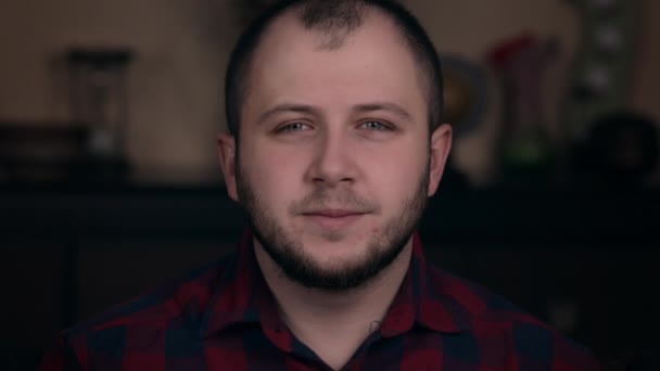 Joyful and smiling young guy of European appearance sits in a chair in a plaid shirt shows a like and respect into camera — ストック動画