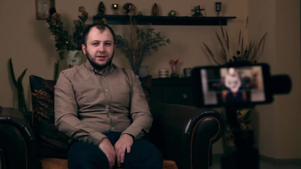 Ο σημαίνων Γενειοφόρος Νεαρός, ένας blogger, ευρωπαϊκής εμφάνισης, κάθεται σε μια καρέκλα με ένα πουκάμισο, καταγράφοντας ένα βίντεο στο τηλέφωνο και ζητά να χτυπήσει το κουδούνι, ειδοποίηση — Αρχείο Βίντεο