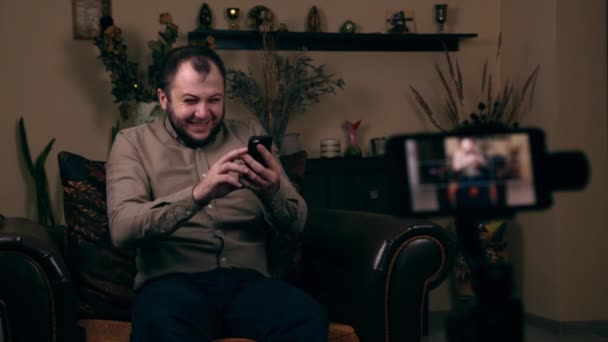 O jovem barbudo influente, um blogueiro, de aparência europeia, senta-se em uma cadeira, grava um vídeo vlog, ri e se comunica com os assinantes. Social Media Blogging Concept — Vídeo de Stock