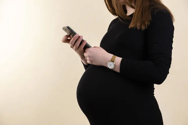 Young pregnant woman on black dress holds her belly and looks at — Stok fotoğraf
