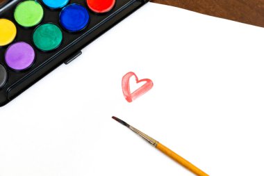 Resim yapmak için fırça ve suluboya boya, kalbi olan bir kağıt. Sevgililer Günü konsepti.