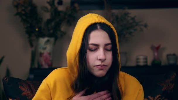 A young girl in a yellow jacket sits on a chair and coughs. Young woman coughs and sneezes female has coronavirus covid-19 symptoms. — Stock Video
