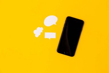 Sarı arka planda kağıt konuşma baloncukları olan akıllı telefonlar. İletişim konsepti. Üst Manzara. Uzayı kopyala Kağıt bileşimi