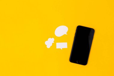 Sarı arka planda kağıt konuşma baloncukları olan akıllı telefonlar. İletişim konsepti. Üst Manzara. Uzayı kopyala Kağıt bileşimi