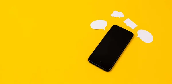 Smartphones with paper speech bubbles on yellow background. Communication concept. Top view. Copy space. Paper composition