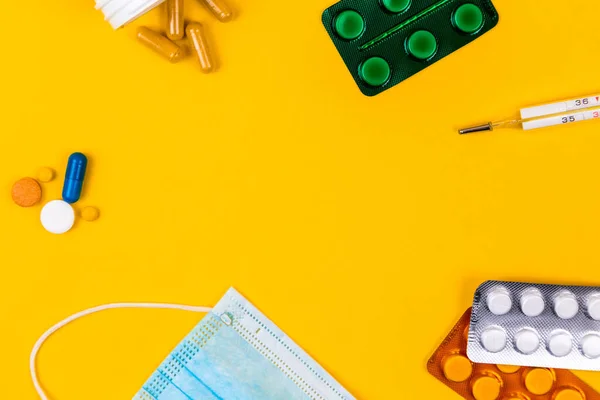 Blue cotton medical protection face mask on a yellow paper background with pills. Coronavirus disease. Corona virus concept. Healthcare and medical concept.