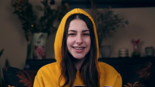 Avrupalı görünümlü genç bir kız gülümseyip elini sallıyor. Selamlama konsepti, keyifli buluşma. Sarı kapüşonlu ceket.. — Stok video