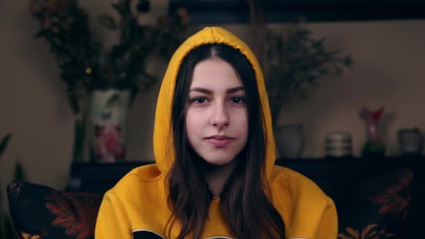 Ένα κοντινό πλάνο μιας νεαρής Ευρωπαίας με ένα κίτρινο μπουφάν με κουκούλα δείχνει μια χειρονομία με τα δάχτυλά της μίνι καρδιά. Η έννοια της αγάπης και των σχέσεων — Αρχείο Βίντεο