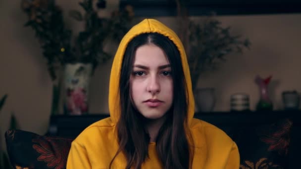 Młoda dziewczyna mruga lub bawi się brwiami. Emocje młodej Europejki z bliska, która siedzi w żółtej bluzie z kapturem. — Wideo stockowe