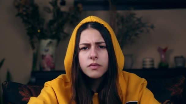 Δυσαρεστημένη και αγανακτισμένη κοπέλα κοιτάζει την κάμερα. Κοντινό πλάνο μιας Ευρωπαίας με κίτρινο μπουφάν και κουκούλα. Η έννοια των συναισθημάτων — Αρχείο Βίντεο