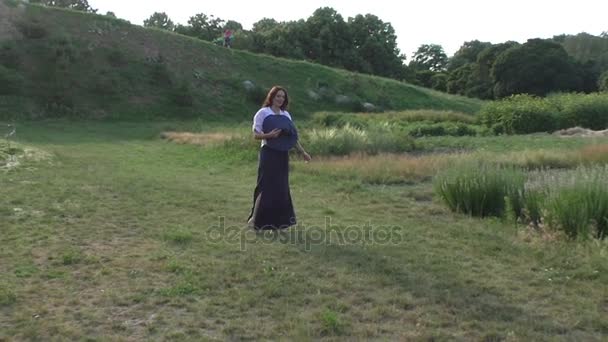 Mujer con un sombrero grande está caminando por la hierba en un prado . — Vídeos de Stock