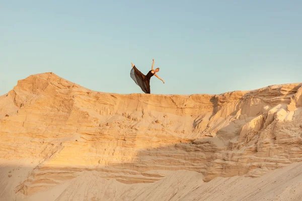 Woman dances high on a sand dune.