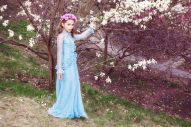 Manolya ağacının yanında güzel bir genç kız. Kafasında bir çiçek çelengi var..