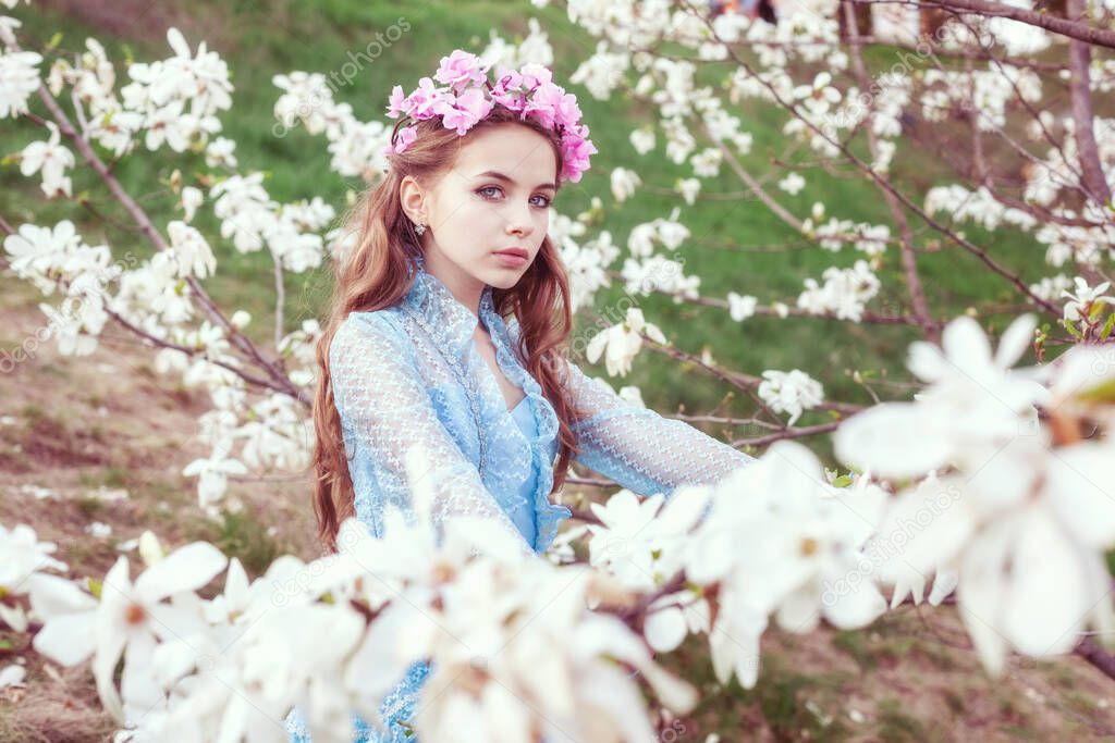 Portrait of an attractive young girl among blooming magnolia trees in the garden.