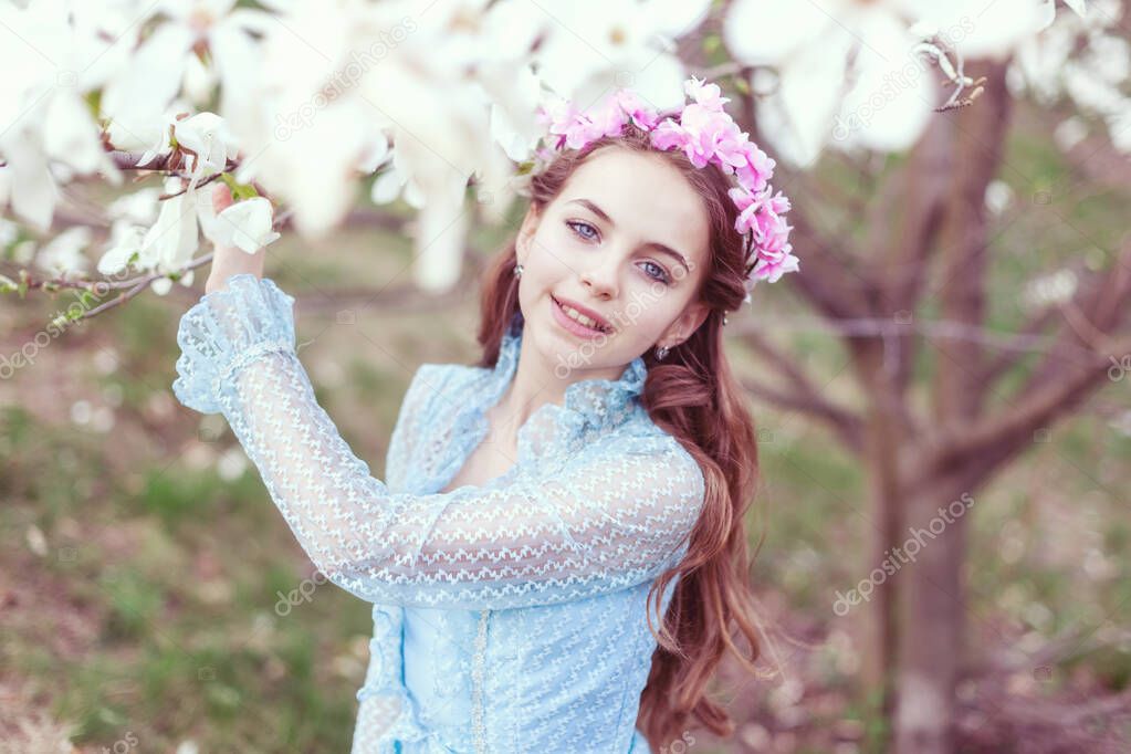 Cute girl with blue eyes stands near the magnolia tree and smiles.
