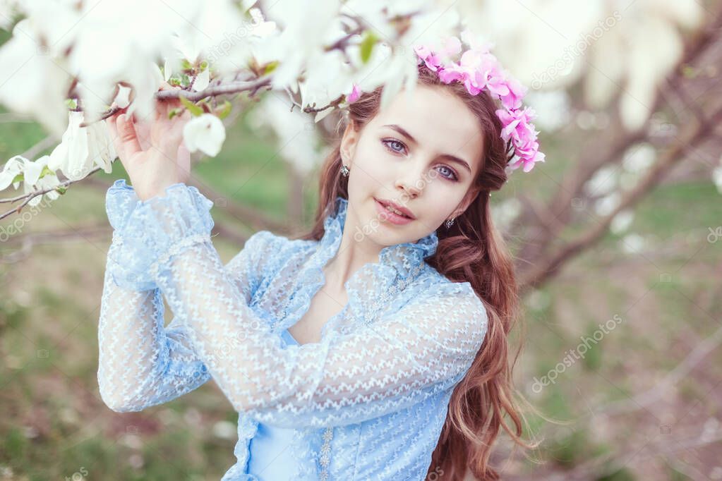 Portrait of a beautiful girl with blue eyes among blooming magnolias.