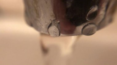 Paslı eski musluktan lavaboya akan su. Ön planda hava kabarcıklı bir damla. Arkaplan bulanık.