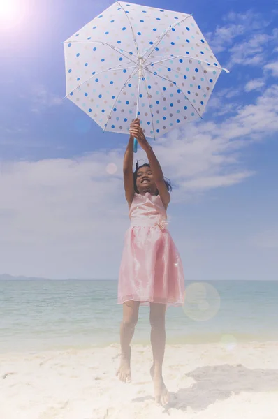 Regenschirm kleines Mädchen springt auf dem Sand und blauem Himmel — Stockfoto