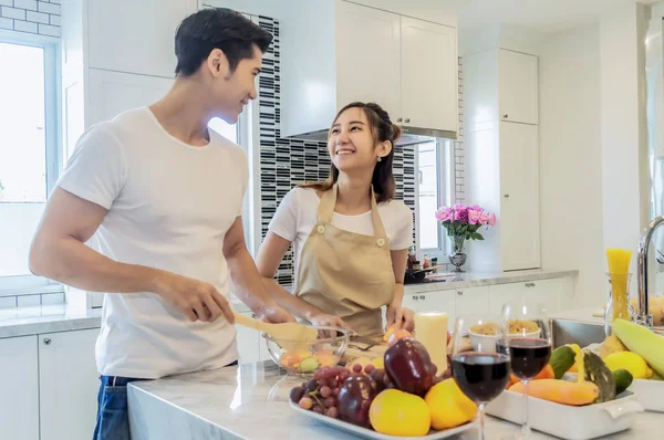 Asiatisches junges Paar schaut und lächelt beim Kochen in der Küche Stockfoto