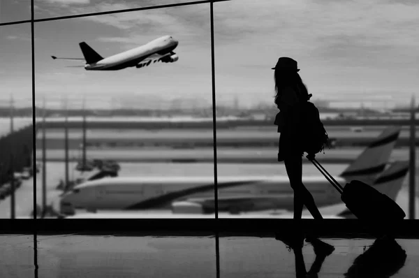 Mujer joven está de pie cerca de la ventana en el aeropuerto y mirando — Foto de Stock