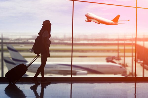 Young woman is standing near window at the airport and watching 