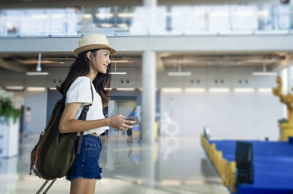 Mujer joven en el aeropuerto a la espera de viajar en avión con un teléfono inteligente . — Foto de Stock