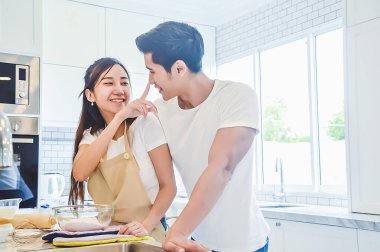 Asyalı çiftler mutfak odasında kek pişirip pişiriyorlar. Kadın ve erkek birbirlerine bakıyorlar..