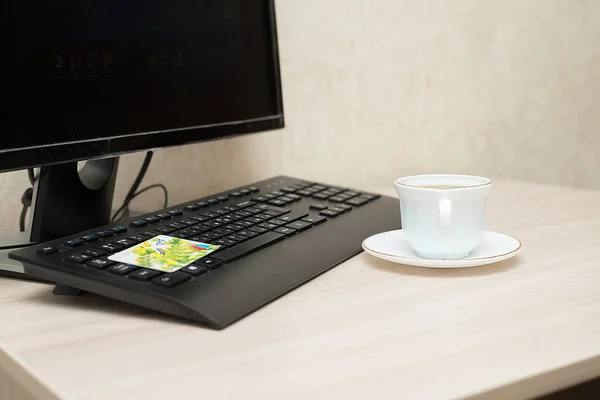 Клавиатура компьютера с чашкой кофе на столе и кредитная карта, которая лежит на клавиатуре — стоковое фото