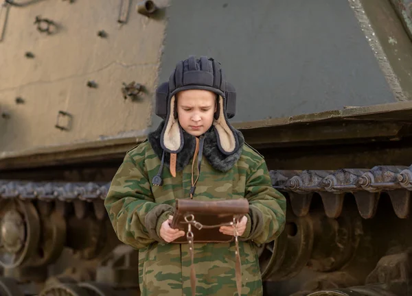 boy in a tanker uniform near a tank with a bag in his hands in peacetime February 23rd holiday day in Russia