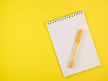 Sarı arka planda beyaz bir not defteri olan sarı kalemler, üst manzara. Not defterli sarı kalem. Kapat.