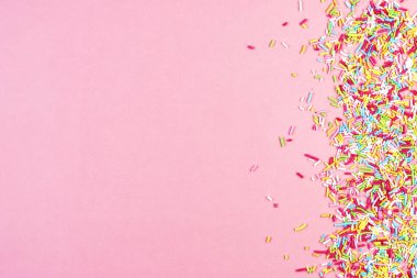 Mutfak pastası gökkuşağı parçacıkları pembe arka plana saçılmış. Pasta süslemek için küçük şeker parçacıkları