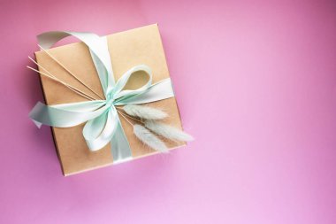 Hediye kutusu ve üstündeki pembe masada bir çiçek. Mavi fiyonklu bir kutu kağıt. yaslanmış biçim.