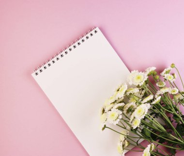 Boş bir not defteri ve pastel pembe arka planda bir çiçek buketi. Mor arka planda papatyalar olan beyaz defter.