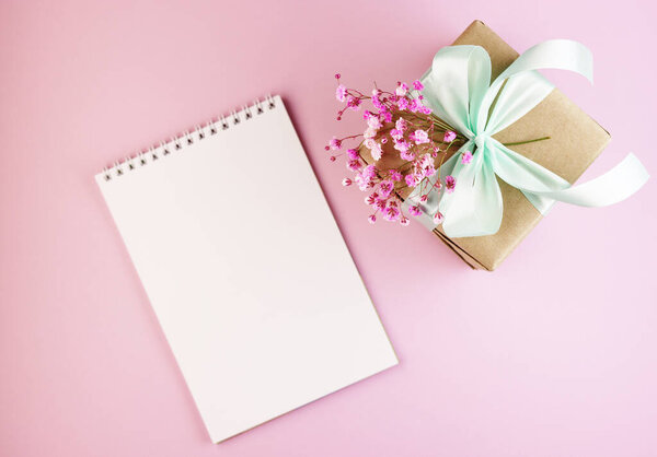 подарочная коробка с букетом весенних цветов на розовом столе. коробка бумаги с голубым бантом на пастельном фоне. flat leumbent style. белый ноутбук рядом с подарком

