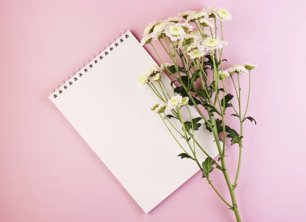 an empty Notepad and a flower bouquet on a pastel pink background. white notebook with daisies on a purple background
