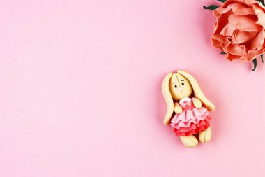 Pembe arka planda plastik Paskalya Tavşanı. Kırmızı çiçeğin yanındaki güzel elbiseli sevimli tavşan.