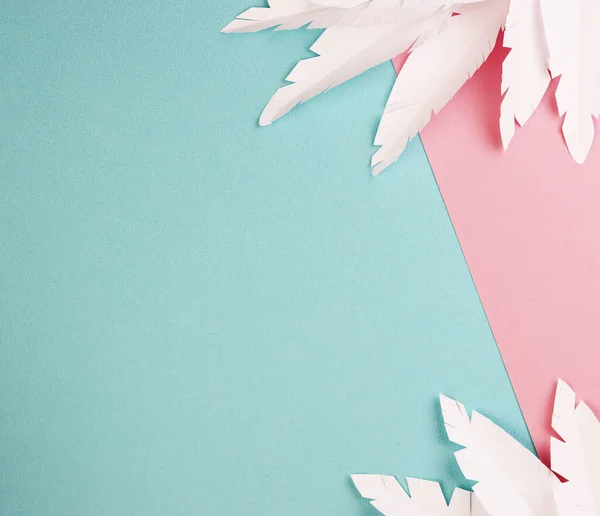 white paper feathers on a pink and blue background, top view. paper decoration on a pastel background