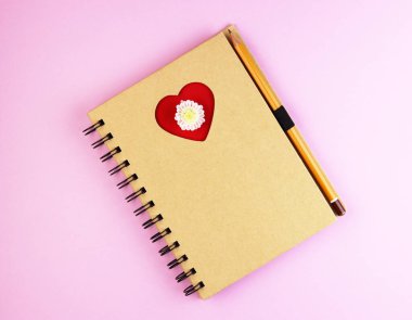 Mavi ahşap masadaki kalemle bir Not Defteri 'nde aşk dolu bir kalp. Kırmızı kalpli kahverengi defter.