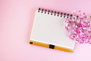 Papatyalar ve pembe arka plan manzaralı boş bir not defteri. Bahar çiçekleri ve masanın üstünde bir defter.